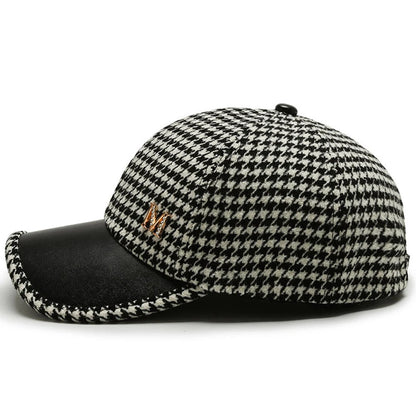Black and white houndstooth baseball cap with black leather brim, gold metal accent, and button top, side view.