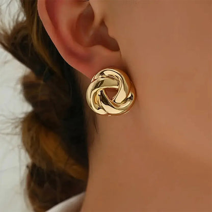 Gold twist knot stud earrings with snap closure worn on woman's ear lobe, chunky geometric design