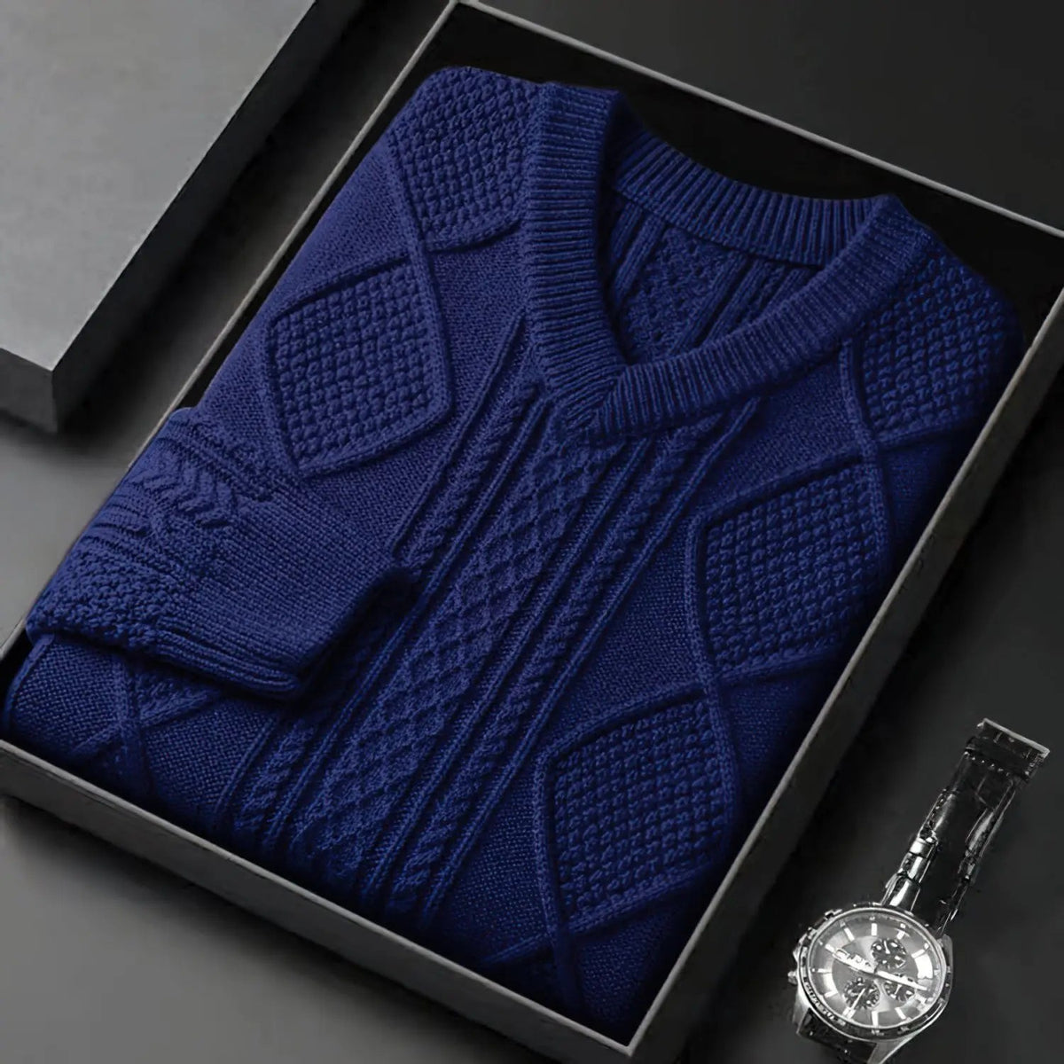 Navy blue cable knit v-neck wool sweater for men, neatly folded in gift box with watch beside it.