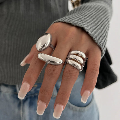 Woman's hand wearing 3 chunky silver adjustable rings from Zephira set, styled with gray ribbed sweater and blue jeans.