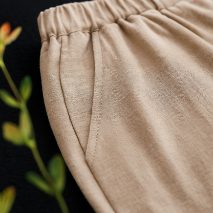 Beige linen tapered pants with elastic drawstring waistband and side pocket detail, close-up view.