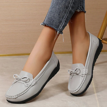Women's gray leather slip-on loafers with bow detail and black sole, paired with distressed denim jeans