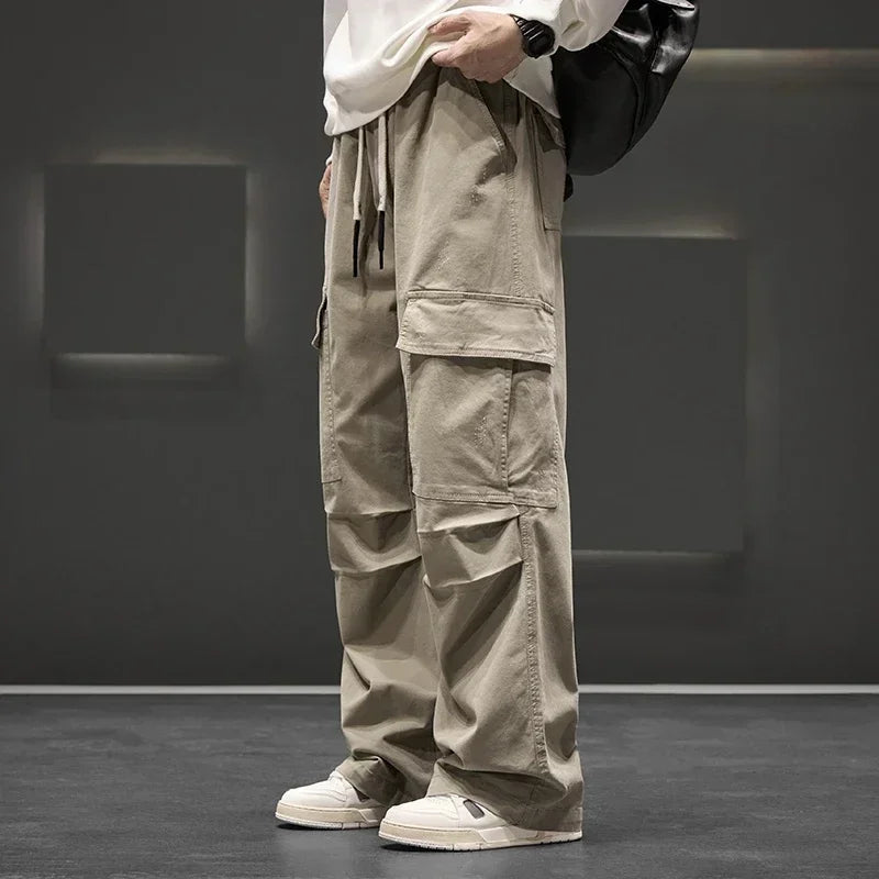 Men's wide-leg khaki cargo pants with large side pockets, elastic drawstring waist, paired with white sneakers and tee.