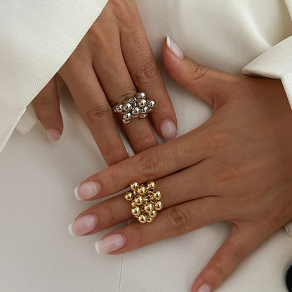 Woman's hand wearing two adjustable beaded cluster rings in silver and gold on white blazer background.