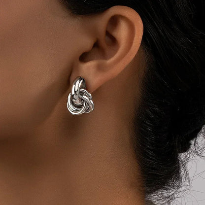 Silver interlocked knot stud earrings worn on a woman's ear, showing chunky twisted loop design with polished finish.