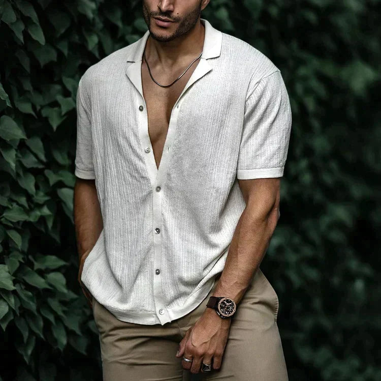 Man wearing white short sleeve button-down linen shirt, open collar, paired with khaki pants and brown watch.