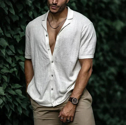Man wearing white short sleeve button-down linen shirt, open collar, paired with khaki pants and brown watch.