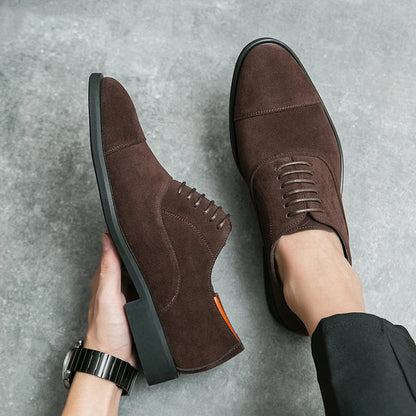 Dark brown suede cap-toe Oxford dress shoes with lace-up closure and rubber sole, shown on foot and in hand.