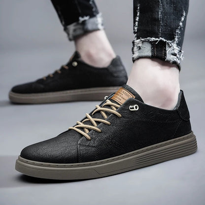 Black leather low-top men's sneakers with tan laces and brown sole, styled with ripped jeans on gray background.