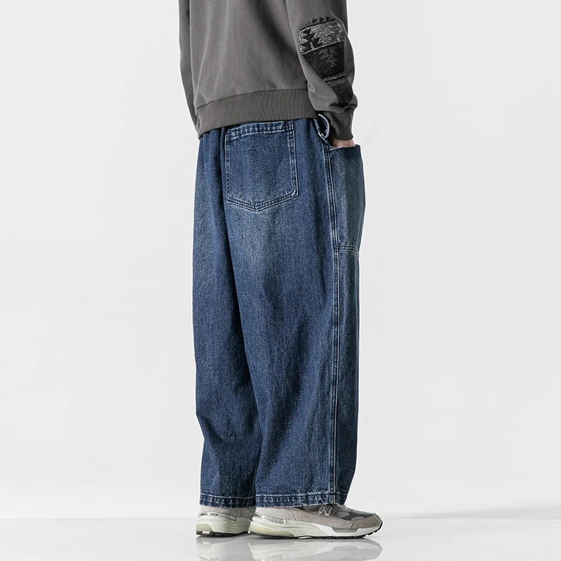 Man wearing relaxed wide-leg blue denim jeans paired with gray sweatshirt and gray sneakers, side view.
