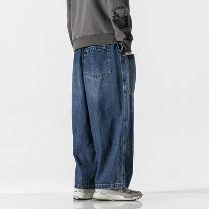 Man wearing relaxed wide-leg blue denim jeans paired with gray sweatshirt and gray sneakers, side view.