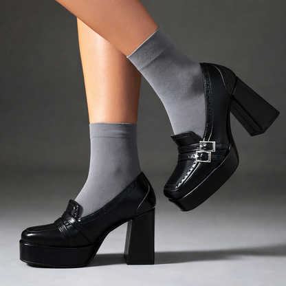 Black patent platform block heel loafers with double buckle detail, styled with gray crew socks on a model.