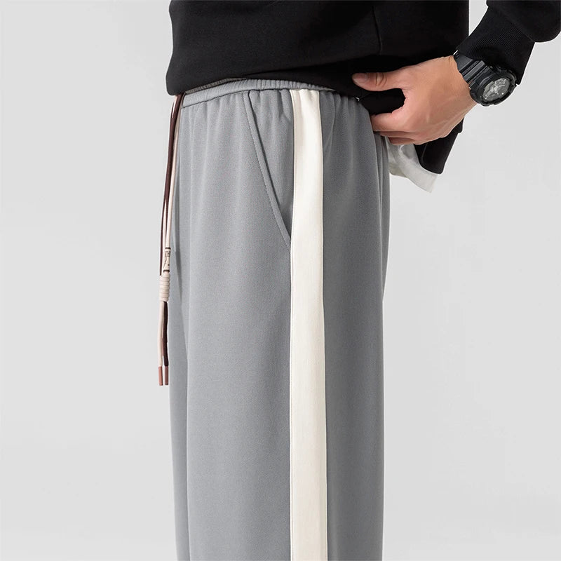 Gray wide-leg men's sweatpants with white side stripe, elastic waistband, drawstring, and side pocket, paired with black sweatshirt