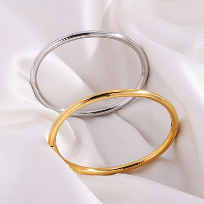 Two minimalist bangle bracelets in gold and silver tones displayed on white satin fabric, smooth polished finish.