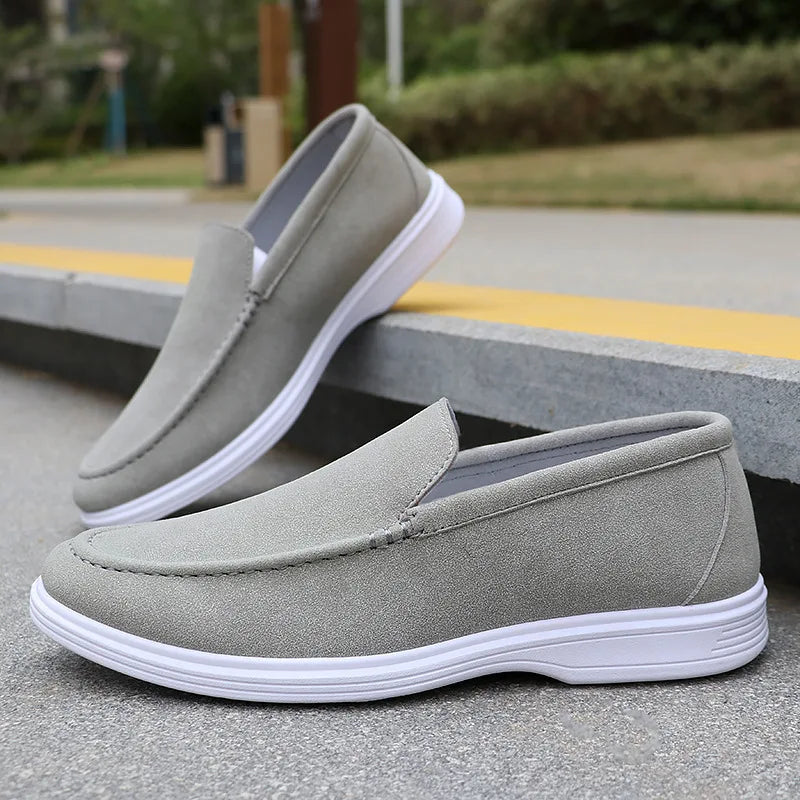Gray suede men's slip-on loafers with white rubber sole, displayed on concrete steps outdoors