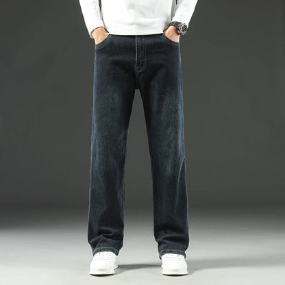 Man wearing dark blue straight leg stretch denim jeans with white sneakers and white sweater, front view.