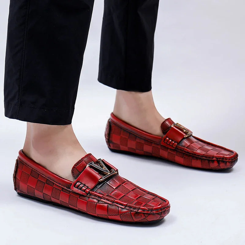Red checkered slip-on loafers for men with gold metal buckle detail, worn with black trousers on white background
