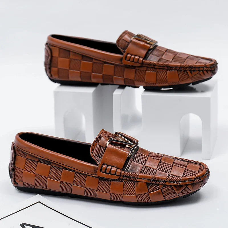 Brown checkered leather slip-on loafers for men with metal LV-style buckle detail, displayed on white blocks