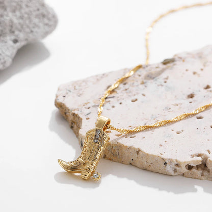 Gold western cowboy boot charm necklace with crystal accents on a twisted chain, displayed on a stone surface.