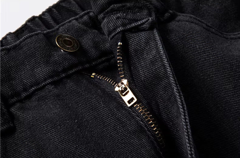 Close-up of black relaxed-fit men's denim jeans showing gold metal zipper and button waistband detail