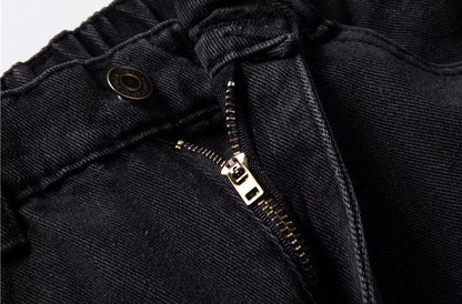 Close-up of black relaxed-fit men's denim jeans showing gold metal zipper and button waistband detail
