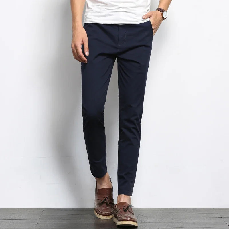 Navy blue slim fit cotton chino pants worn with white tee and brown loafers, tapered ankle length style