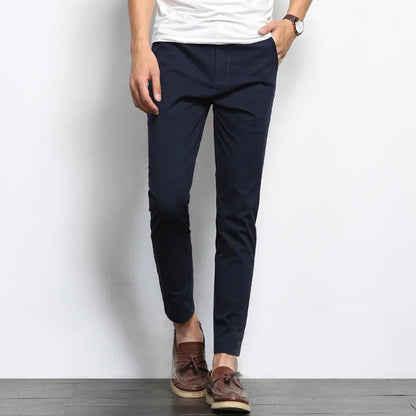 Navy blue slim fit cotton chino pants worn with white tee and brown loafers, tapered ankle length style