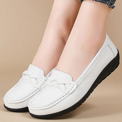 White leather women's slip-on loafers with braided detail and black rubber sole, shown on feet with denim jeans.