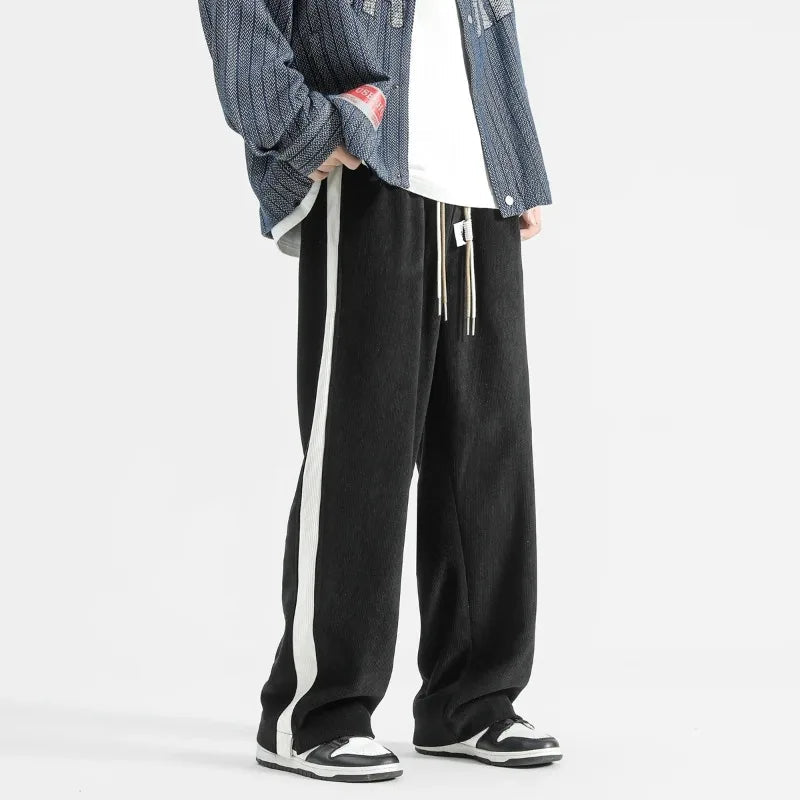 Black wide-leg corduroy drawstring joggers with white side stripe, styled with blue textured jacket and white sneakers