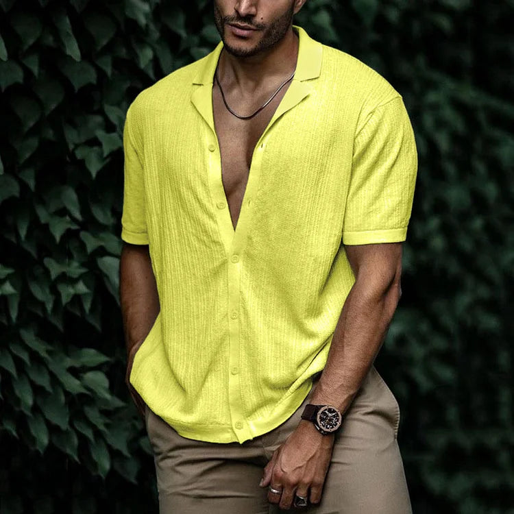 Man wearing a neon yellow short sleeve button-down shirt with khaki pants and a watch, posed outdoors.