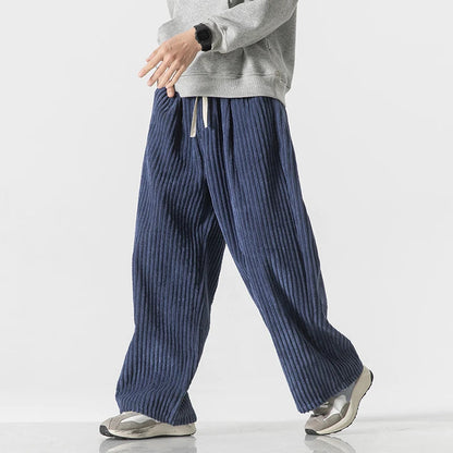 Men's wide-leg navy blue corduroy drawstring pants paired with gray sweatshirt and gray sneakers, casual streetwear style