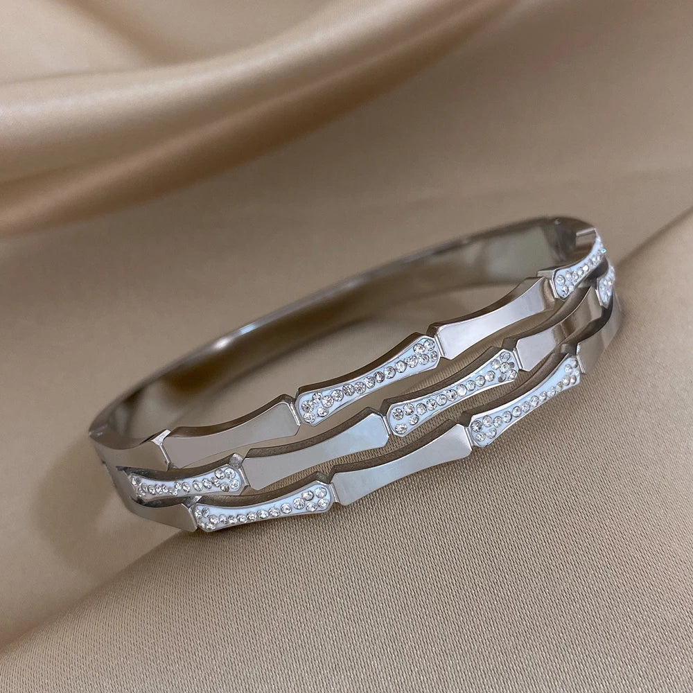 Silver tone geometric bangle bracelet with crystal rhinestone accents on satin fabric background