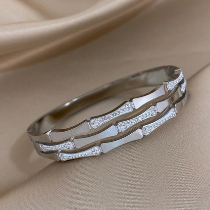 Silver tone geometric bangle bracelet with crystal rhinestone accents on satin fabric background