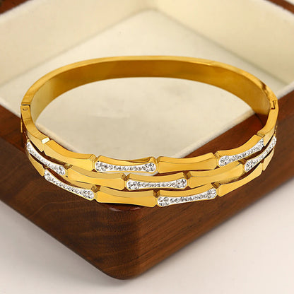 Gold tone bangle bracelet with geometric links and sparkling white crystal accents displayed in a wooden jewelry box.