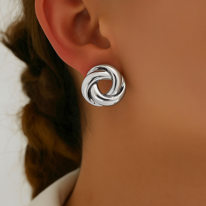 Silver twisted knot stud earrings worn on a woman's ear, featuring interlocking circular design with polished finish.