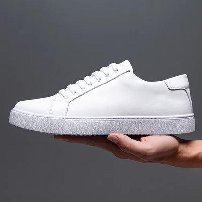 White leather lace-up men's sneakers with flat rubber sole, held in hand against gray background, low-top casual style