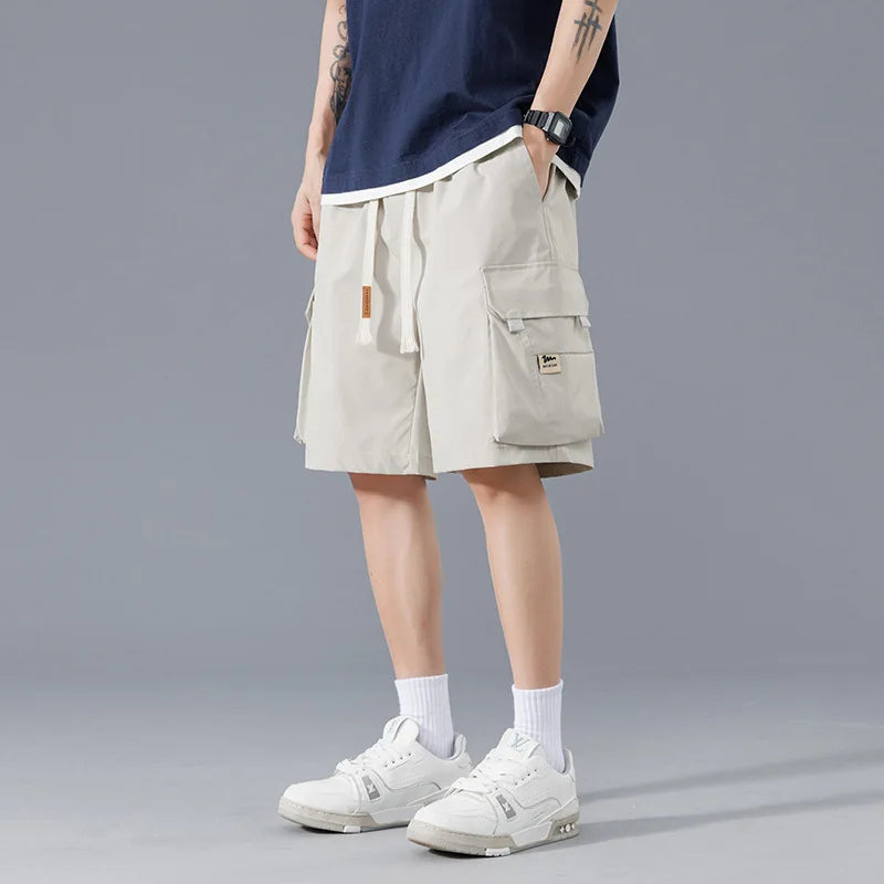 Men's beige cargo shorts with drawstring waist and side pockets, styled with navy tee and white sneakers