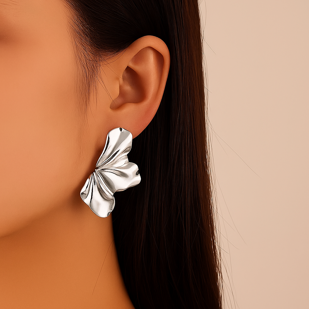 Silver ruffled statement stud earrings with textured wavy petal design worn on woman's ear, side profile view