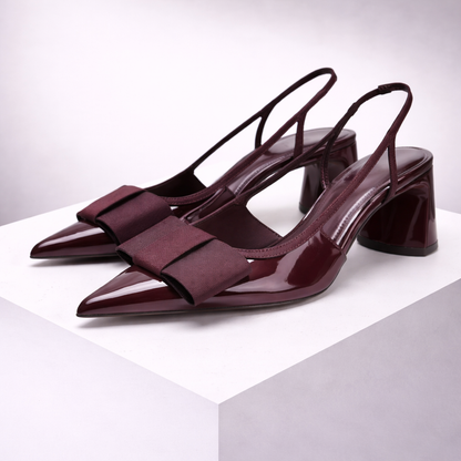 Women's burgundy pointed-toe patent leather slingback heels with bow detail and block heel on white display