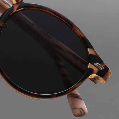Close-up of round tortoiseshell sunglasses with dark tinted lenses and marbled brown acetate frame and temples