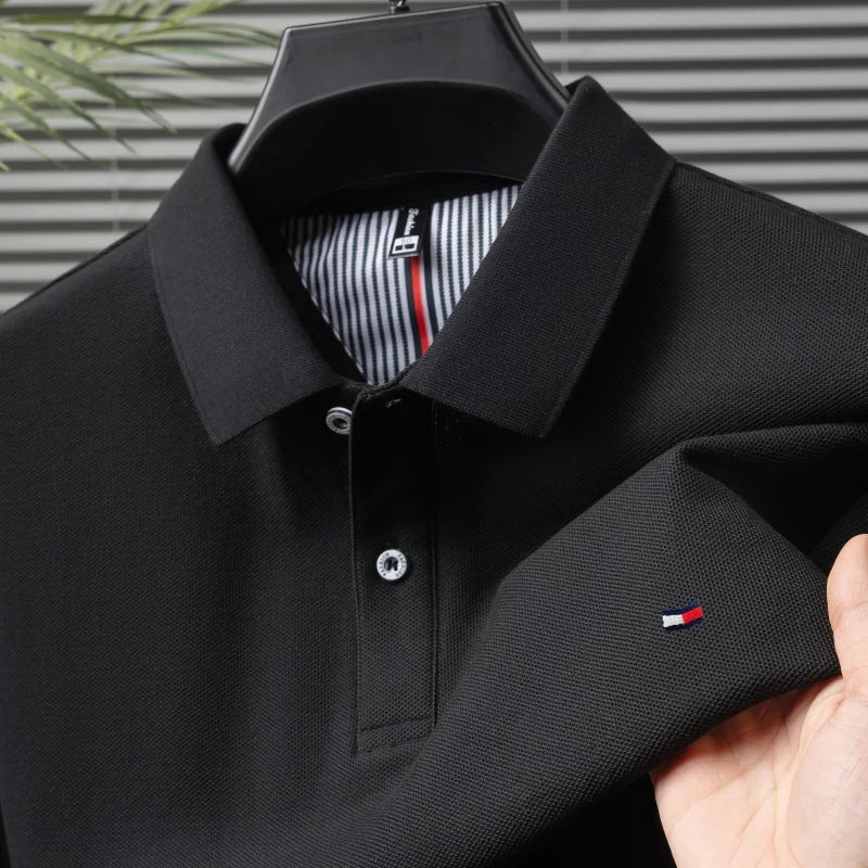 Black men's cotton polo shirt on hanger with striped collar lining, silver buttons, and small flag logo embroidery on chest.