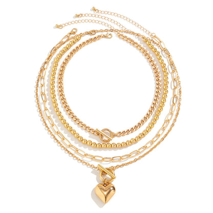 Gold layered necklace set featuring curb chain, bead strand, paperclip chain, and heart pendant with toggle clasp