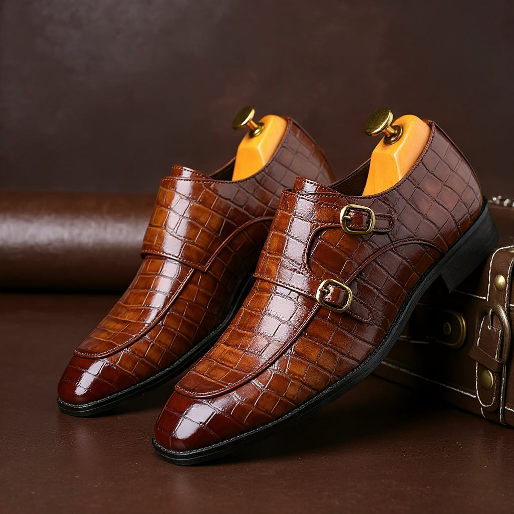 Brown crocodile-embossed leather men's double monk strap dress shoes with gold buckles and shoe trees inserted.