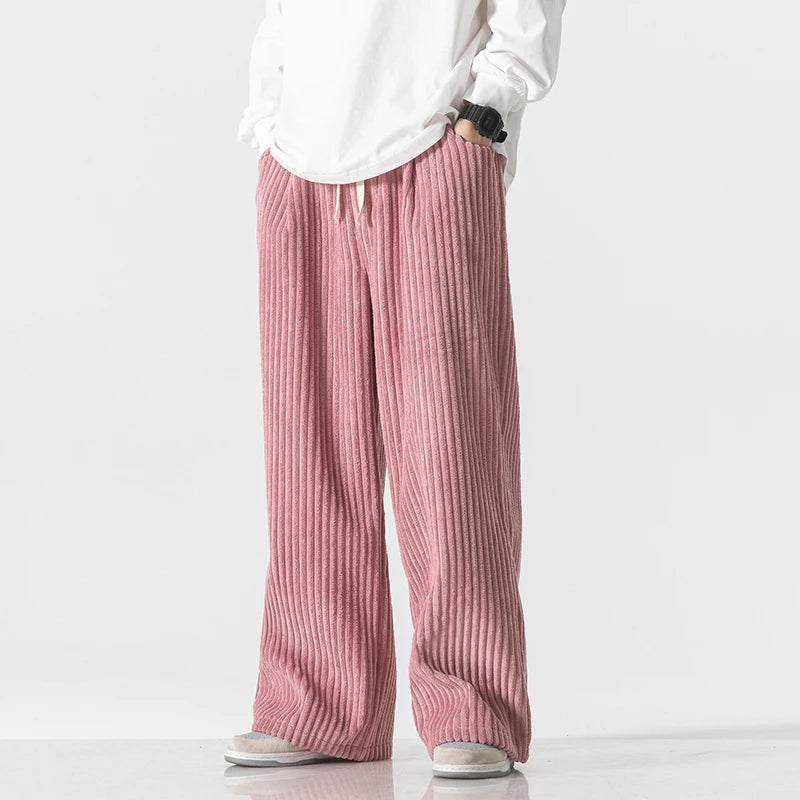 Men's pink wide-leg corduroy drawstring pants with vertical ribbed texture, paired with white oversized top and gray sneakers.