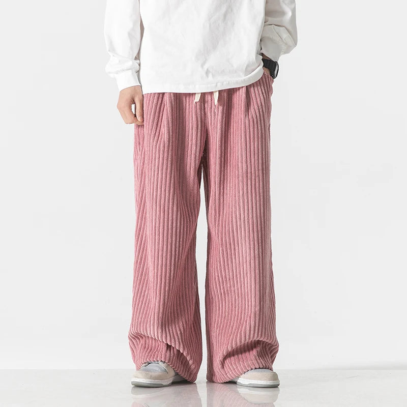 Men's wide-leg pink corduroy drawstring pants with ribbed texture, paired with white top and gray sneakers