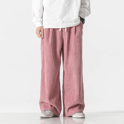 Men's wide-leg pink corduroy drawstring pants with ribbed texture, paired with white top and gray sneakers