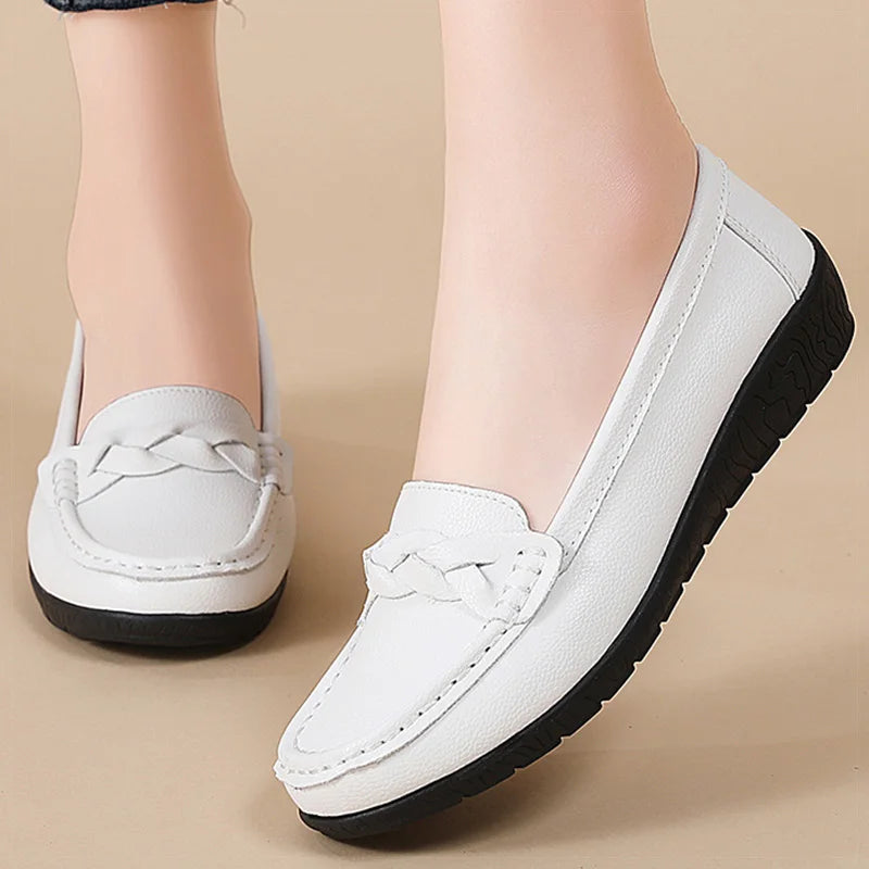 White women's leather slip-on loafers with braided detail and black rubber sole, shown on feet against beige background.