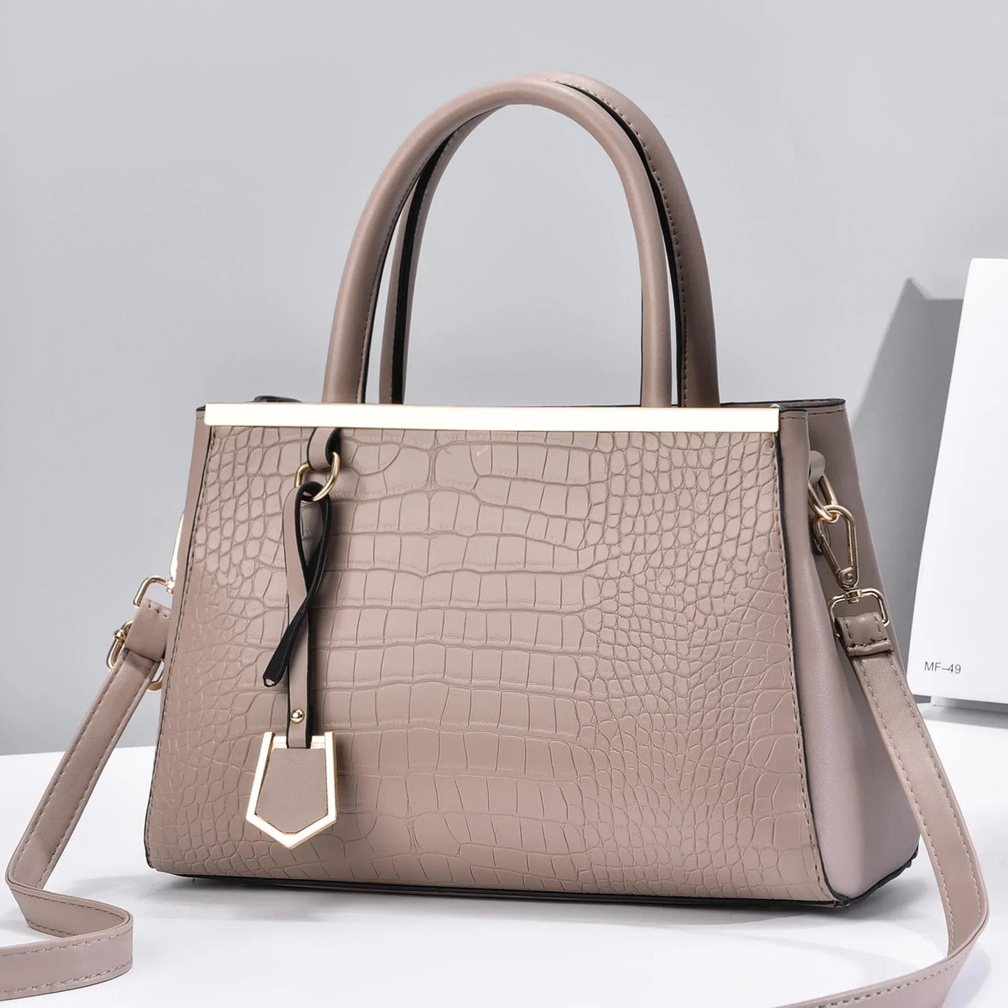 Taupe croc-embossed structured handbag with dual top handles, gold-tone hardware, charm pendant, and removable crossbody strap.