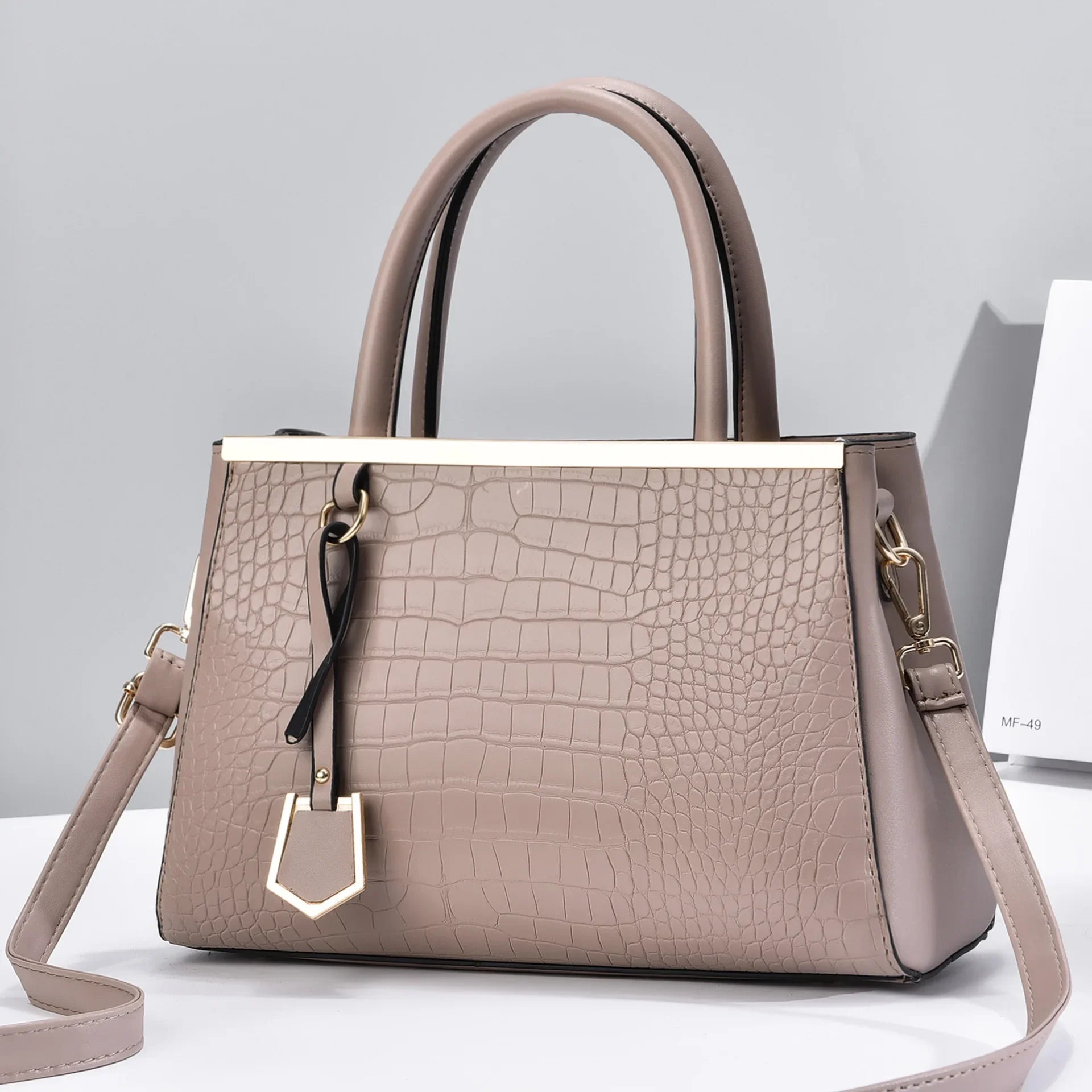 Taupe croc-embossed structured handbag with dual top handles, gold-tone hardware, charm pendant, and removable crossbody strap.