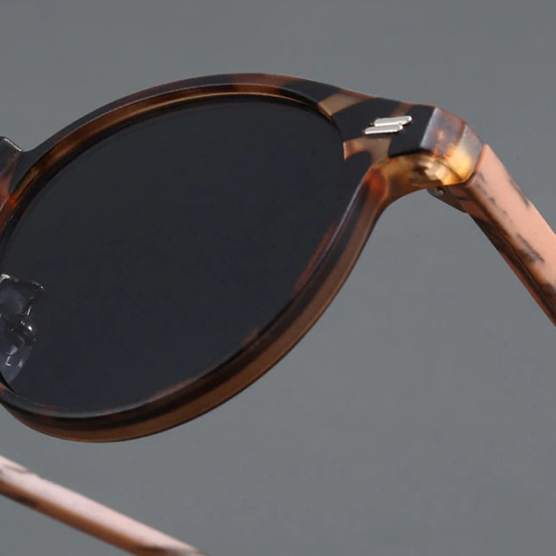 Close-up of round tortoiseshell sunglasses with dark polarized lenses and silver hinge hardware on gray background
